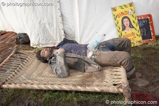 A man caked in mud sleeps uncomfortably on a small seating platform outside the Bedouin Cafe at Glade Festival 2007. Aldermaston, Great Britain. © 2007 Photographicon