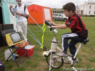 A boy pedals to generate power for an old-style TV video game at the London Green Lifestyle Show 2005. Great Britain. © 2005 Photographicon