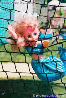 A barbie doll dressed as a mermade is causght in a fishing net at Big Green Gathering 2003. Cheddar, Great Britain. © 2003 Photographicon