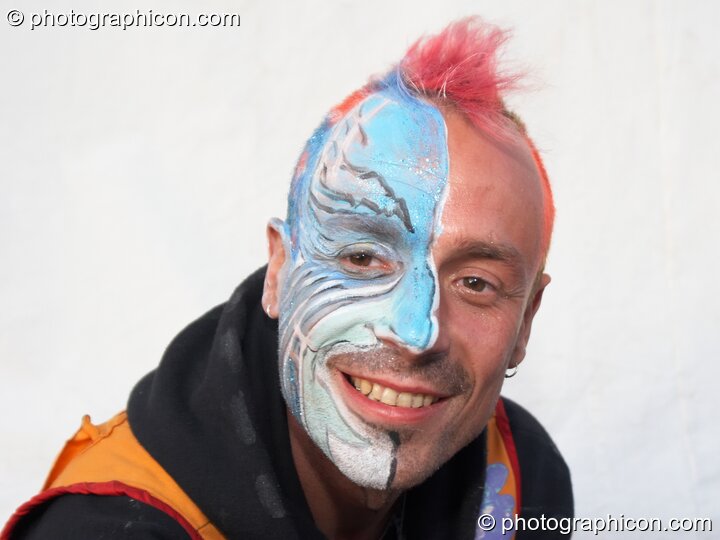 Grinning man with half his face painted at Big Green Gathering 2005. Burrington, Cheddar, Great Britain. © 2005 Photographicon