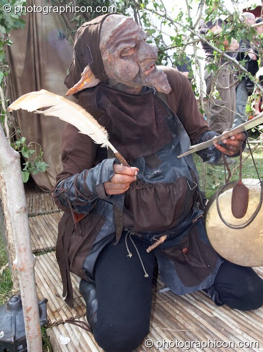 A person in a goblin costume nakes notes with a feather quill pen at Big Green Gathering 2007. Burrington, Cheddar, Great Britain. © 2007 Photographicon