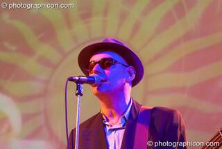 A member of the Alabama 3 stands in front of a projected sun motive with his Blues Brothers costume illuminated by blue light while performing on the Glade Stage at Glade Festival 2006. Aldermaston, Great Britain. © 2006 Photographicon