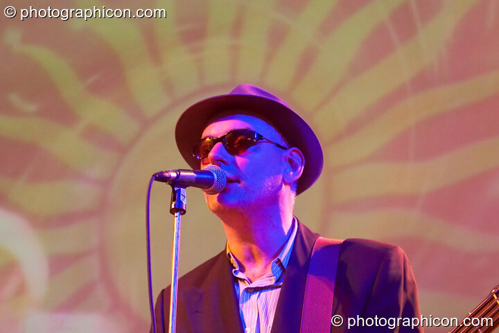 A member of the Alabama 3 stands in front of a projected sun motive with his Blues Brothers costume illuminated by blue light while performing on the Glade Stage at Glade Festival 2006. Aldermaston, Great Britain. © 2006 Photographicon