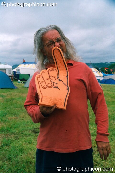 Professor Des Kay picks his nose with a giant hand at Glastonbury Festival 2002. Pilton, Great Britain. © 2002 Photographicon