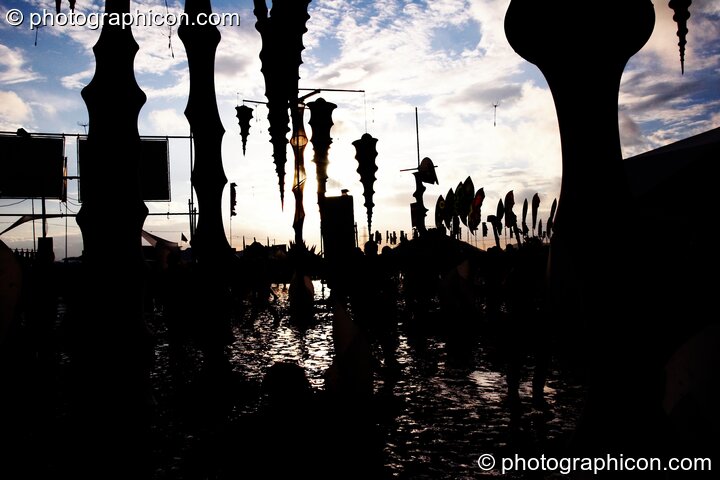The sun reflects off the mud, silhouetting hanging decor in the ID Spiral arena of the Dance Village at Glastonbury Festival 2007. Pilton, United Kingdom. © 2007 Photographicon