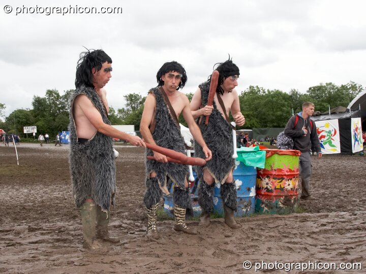 The men dressed as cavemen wander through the mud at Glastonbury Festival 2007. Pilton, United Kingdom. © 2007 Photographicon