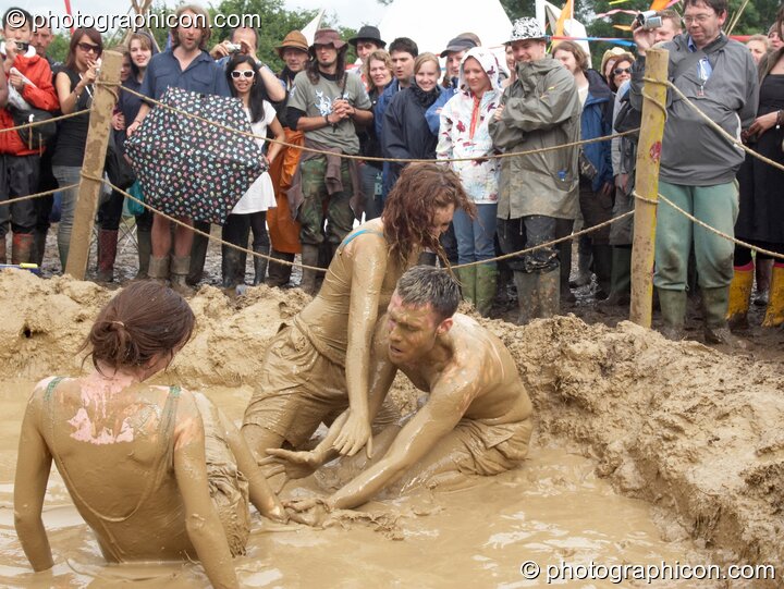 Two women and a man wrestle in a mud pit in the Tipi Field at Glastonbury Festival 2007. Pilton, Great Britain. © 2007 Photographicon