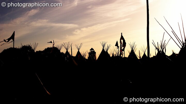 Silhouetted against the setting sun, the distant Park Tower nestles amongst tipis in the Tipi Village at Glastonbury Festival 2008. Pilton, Great Britain. © 2008 Photographicon
