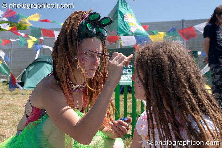 One woman wearing welding glasses paints the face of another at Glastonbury Festival 2004. Pilton, Great Britain. © 2004 Photographicon