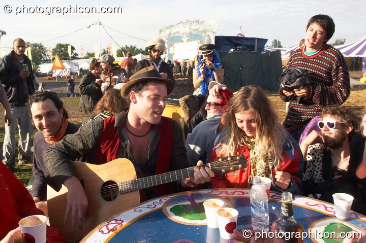 A group of wonky people gather round a table for a jam in the early morning sun at the Secret Garden Party 2007. Huntingdon, Great Britain. © 2007 Photographicon