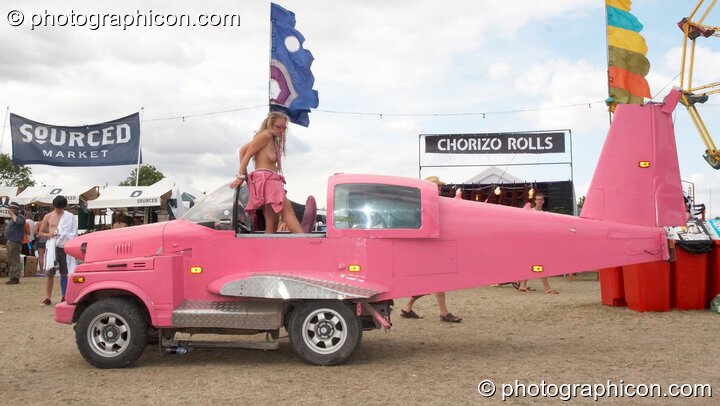 A topless woman stands in a pink aircraft/car hybrid at the Secret Garden Party 2010. Huntingdon, Great Britain. © 2010 Photographicon