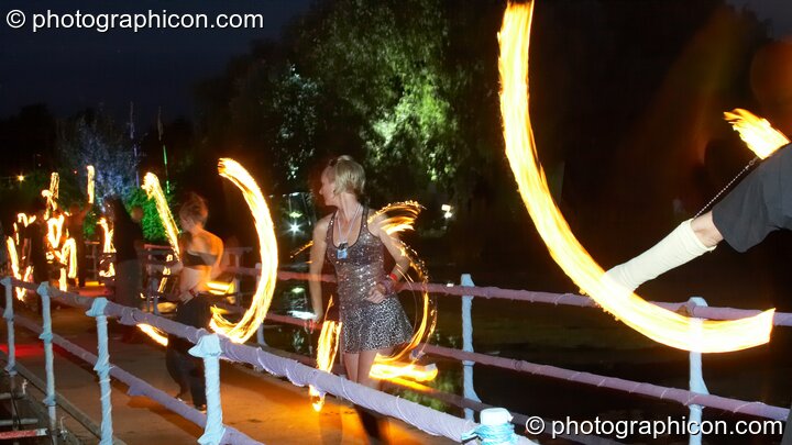 A line of fire-poi spinners on the bridge watch the burning Galleon at the Secret Garden Party 2008. Huntingdon, Great Britain. © 2008 Photographicon