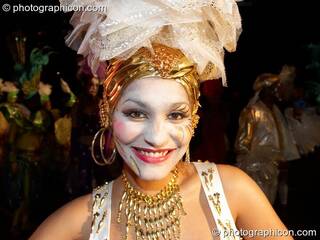 Woman with while face, gold jewellery and tall layer-hat smiles during the carnival at the Thames Festival 2005. London, Great Britain. © 2005 Photographicon