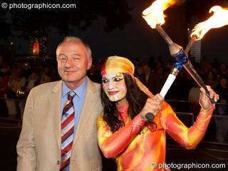 Ken Livingston (Mayor of London) is eyed by woman in leotard holding crossed fire sticks during the opening of the night carnival at the Thames Festival 2005. Great Britain. © 2005 Photographicon
