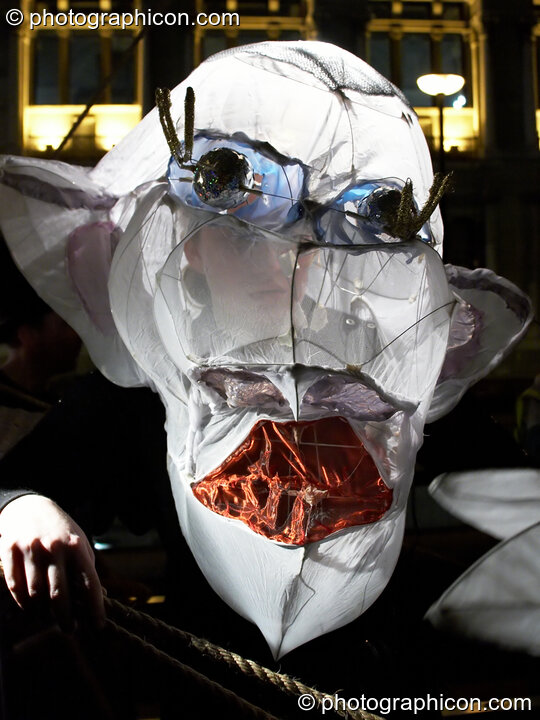 Person wearing a large paper carnival mask of disfigured head at the Thames Festival 2005. London, Great Britain. © 2005 Photographicon