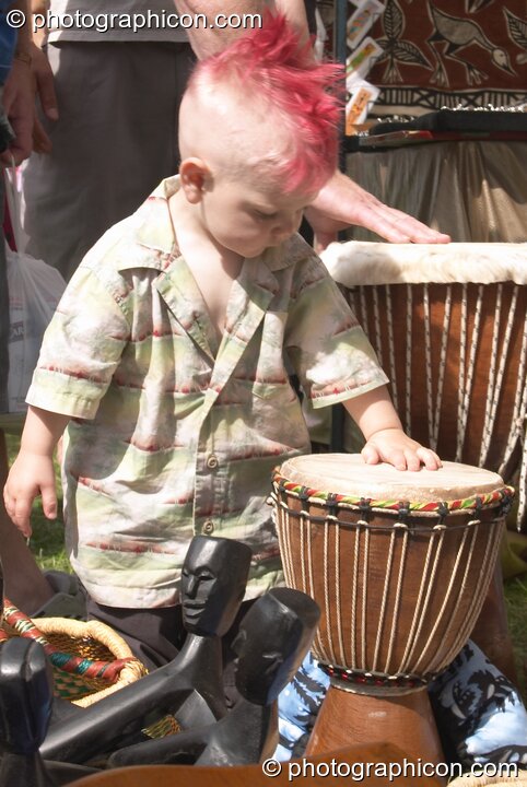Small child with punk-style haircut plays with a drum on a stall at Kingston Green Fair 2004. Kingston Upon Thames, Great Britain. © 2004 Photographicon