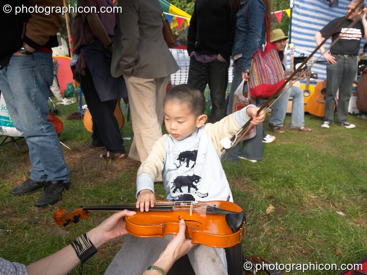 Surrey Strings encourages a child to play violin at Kingston Green Fair 2005. Kingston Upon Thames, Great Britain. © 2005 Photographicon