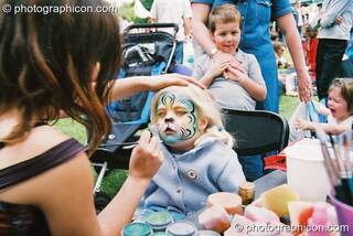 A young girl has her face professionally painted as a cat at Kingston Green Fair 2003. Kingston upon Thames, Great Britain. © 2003 Photographicon