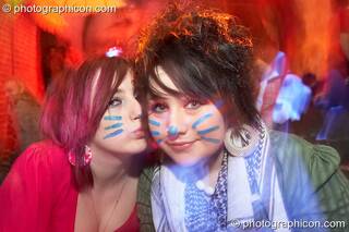 Two cute women with fluro painted wiskers kiss in the Kalahari room at The Synergy Project. London, Great Britain. © 2007 Photographicon
