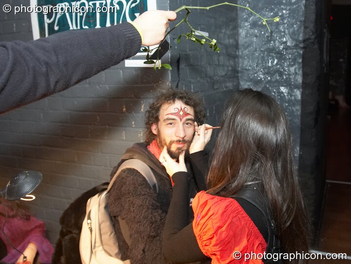 A man has his face painted under a sprig of mistletoe at The Synergy Project. London, Great Britain. © 2007 Photographicon