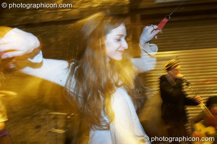 A woman twirls poi to entertain the queue in the tunnel outside at The Synergy Project. London, Great Britain. © 2007 Photographicon