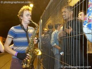 Ewan plays sax to the an audiene the other side of  the smoker's cage in the road tunnel outside The Synergy Project. London, Great Britain. © 2008 Photographicon