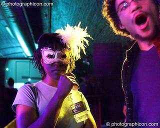A woman in a mask drinks water while her male friend looks on in the entrance space at Luminopolis (formerly The Synergy Project). London, Great Britain. © 2008 Photographicon