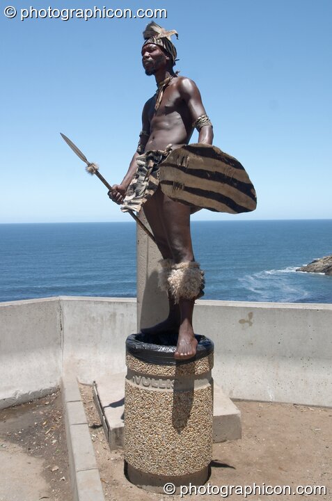 A man in traditional dress stands on a plynth over looking the sea - Western Cape, South Africa. George. © 2005 Photographicon