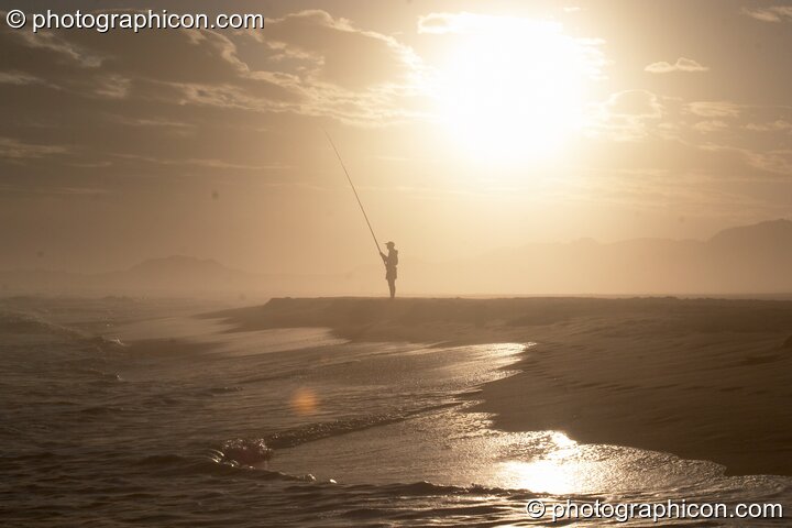 Profile of a distant fisherman with the sun reflected off sea that is lapping onto the beach at Boesmansriviermond - Eastern Cape, South Africa. © 2005 Photographicon