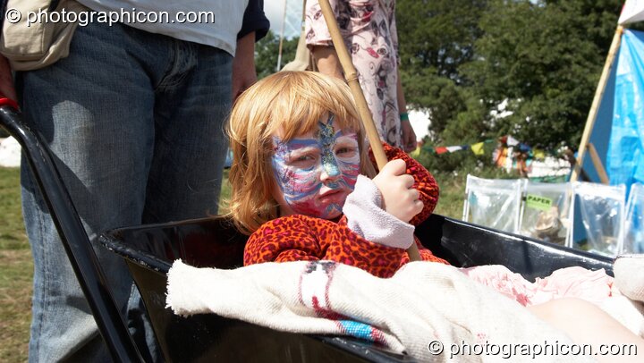 A child being carried in a wheel barrow at Big Green Gathering 2005. Burrington, Cheddar, United Kingdom. © 2005 Photographicon