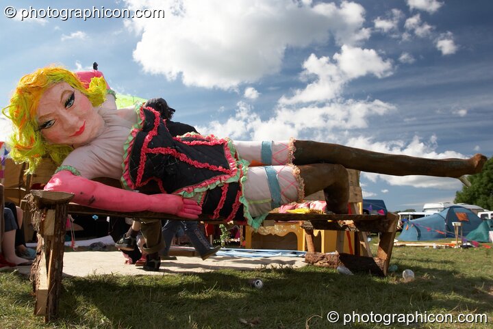 A larger than life paper model of a Burlesque dancer lies on a bench at Big Green Gathering 2005. Burrington, Cheddar, United Kingdom. © 2005 Photographicon