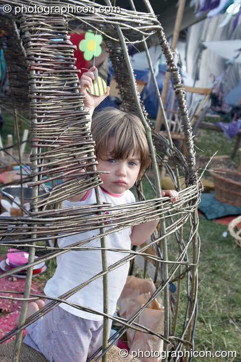 Child stares out from wicker structure at Big Green Gathering 2005. Burrington, Cheddar, United Kingdom. © 2005 Photographicon