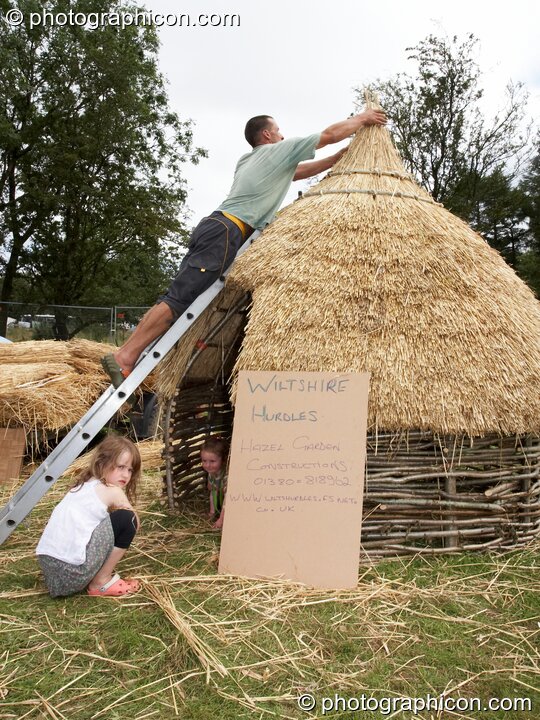 A man straw thatches a small wattle dwelling while his children look on at Big Green Gathering 2007. Burrington, Cheddar, United Kingdom. © 2007 Photographicon