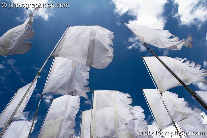 Shot from below, white flags flutter against a deep blue sky and fluffy clouds at Glade Festival 2005. Aldermaston, United Kingdom. © 2005 Photographicon