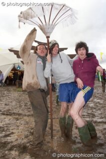 Three guys wade through the mud carrying a large parasol at Glade Festival 2007. Aldermaston, United Kingdom. © 2007 Photographicon