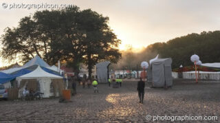 The early morning sun peeks through mist above the trees and illuminates the mud-churned ground at Glade Festival 2007. Aldermaston, United Kingdom. © 2007 Photographicon