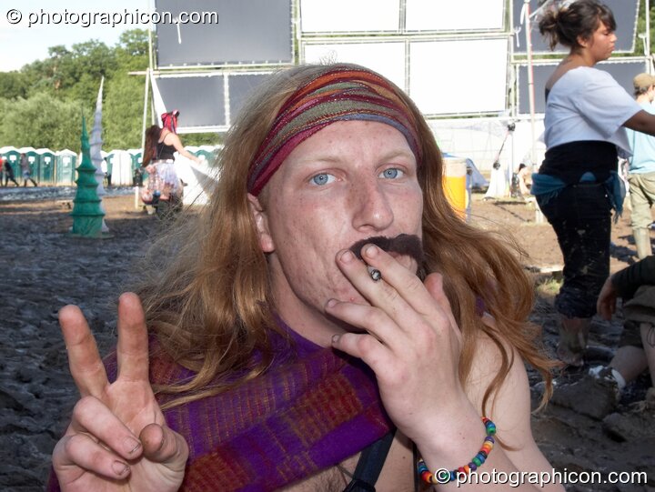 A long haired man with a false moustache smokes a cigarette at Glade Festival 2007. Aldermaston, United Kingdom. © 2007 Photographicon