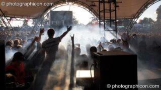 The cheering and waving Glade Stage audience are silhouetted by the Sun and stage smoke at Glade Festival 2007. Aldermaston, United Kingdom. © 2007 Photographicon