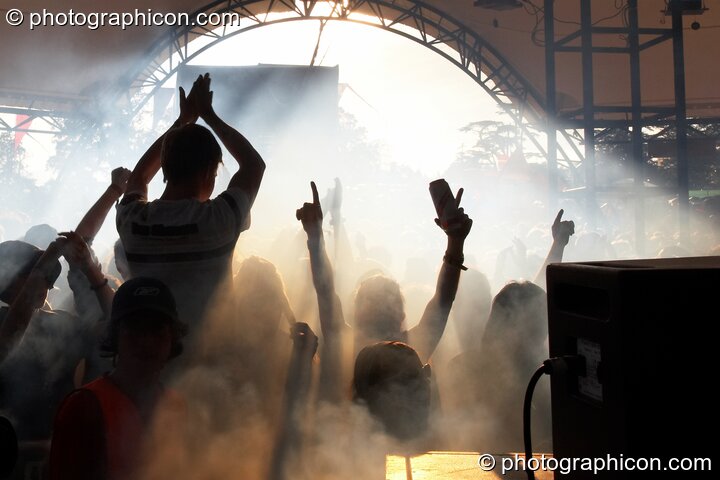 The cheering and waving Glade Stage audience are silhouetted by the Sun and stage smoke at Glade Festival 2007. Aldermaston, United Kingdom. © 2007 Photographicon