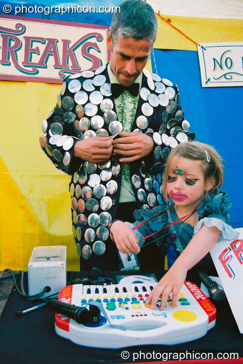 Man and daughter play music for the freak show in the Lost Vagueness field at Glastonbury Festival 2003. Pilton, United Kingdom. © 2003 Photographicon