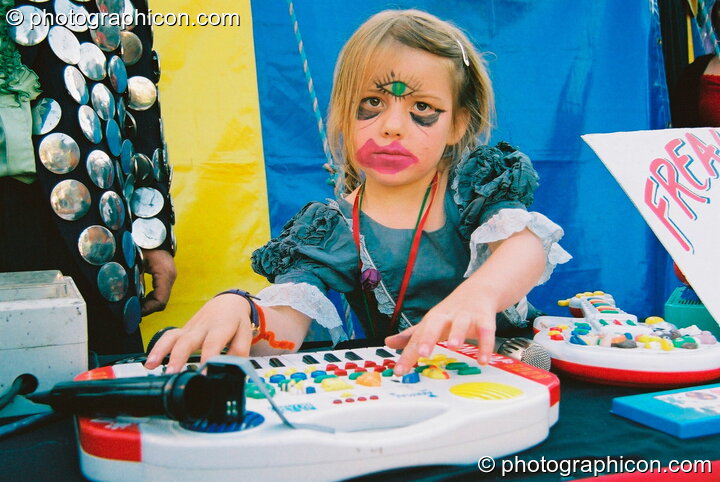 Girl with grotesque make-up plays music for the freak show in the Lost Vagueness field at Glastonbury Festival 2003. Pilton, United Kingdom. © 2003 Photographicon