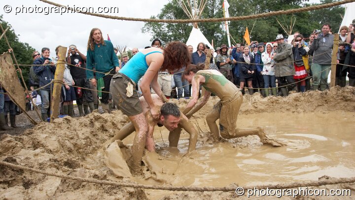 Two women and a man wrestle in a mud pit in the Tipi Field at Glastonbury Festival 2007. Pilton, United Kingdom. © 2007 Photographicon