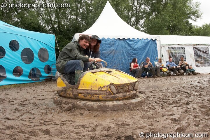 Two people sit in a dodgem car amongst the mud in the Lost Vagueness field at Glastonbury Festival 2007. Pilton, United Kingdom. © 2007 Photographicon