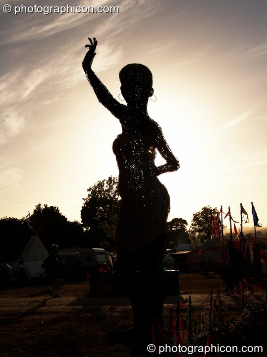Silhouetted against the setting sun, a large wicker statue of a woman in the Craft Field at Glastonbury Festival 2008. Pilton, United Kingdom. © 2008 Photographicon