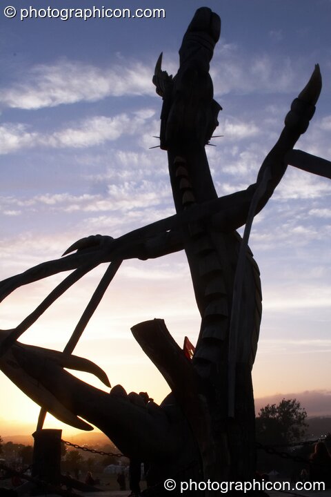 Silhouetted against the setting sun, the Tree Pirates Dragon chainsaw sculpture in the King's Meadow (Sacred Space) at Glastonbury Festival 2008. Pilton, United Kingdom. © 2008 Photographicon