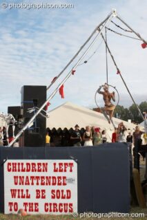 A woman performs acrobatics near a warning sign at the Secret Garden Party 2010. Huntingdon, United Kingdom. © 2010 Photographicon