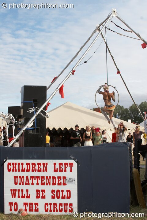 A woman performs acrobatics near a warning sign at the Secret Garden Party 2010. Huntingdon, United Kingdom. © 2010 Photographicon