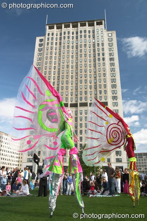 Women wearing bright winged costumes gracefully dance on stilts in front of the Shell Building at the Thames Festival 2004. London, United Kingdom. © 2004 Photographicon