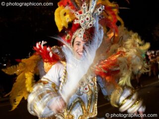 Man in colourful feathery costume finery dances with big white feather participates in the carnival at the Thames Festival 2005. London, United Kingdom. © 2005 Photographicon