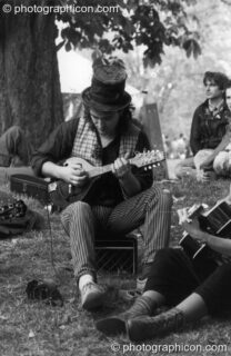 A man plays a relaxing tune under a tree at the first Kingston Green Fair in 1987. Kingston upon Thames, United Kingdom. © 1987 Photographicon